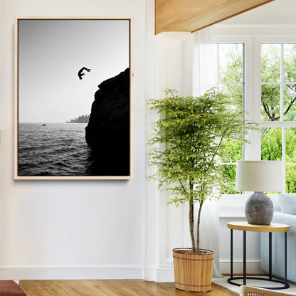 Silhouette of a person mid-air during a cliff jump over the ocean, captured in black and white for minimalist adventure decor.