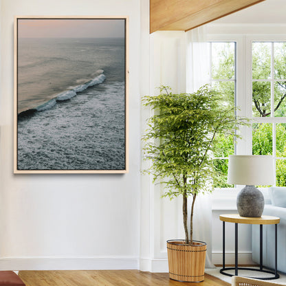 Aerial view of ocean waves rolling towards the shore under a soft sunset sky, creating a peaceful and minimalist coastal scene.