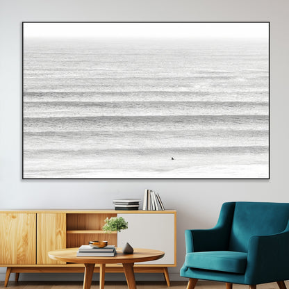 Monochrome photo of a lone surfer in calm layered waves, perfect for minimalist coastal or moody ocean-inspired wall decoration.