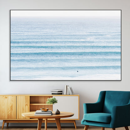 Minimalist ocean view with soft blue waves and a lone surfer, creating a serene and airy coastal aesthetic, perfect for tranquil home decor.