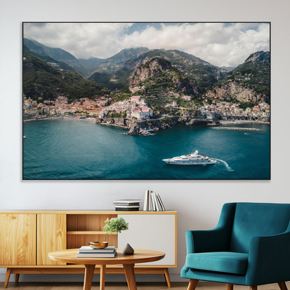 Aerial view of Amalfi Coast, Italy, with colorful hillside houses, lush green mountains, and a luxury yacht sailing in turquoise waters.