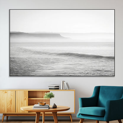 A black and white minimalist seascape featuring soft rolling waves and misty distant cliffs, creating a serene and timeless coastal atmosphere.