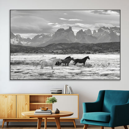 A black and white landscape of wild horses grazing in a vast grassland with towering mountains in the background, creating a moody and rustic western aesthetic.
