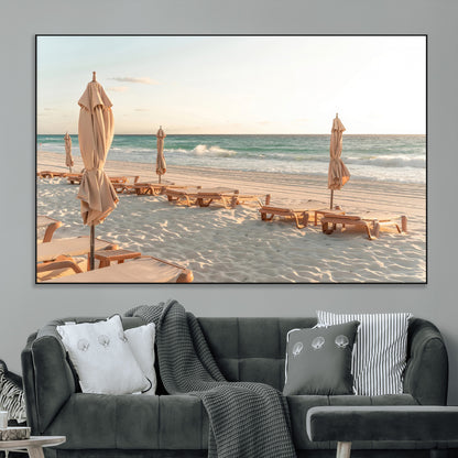 Minimalist photo of empty beach loungers and umbrellas on soft sand, ideal for calm seaside or pastel coastal-style home decor.