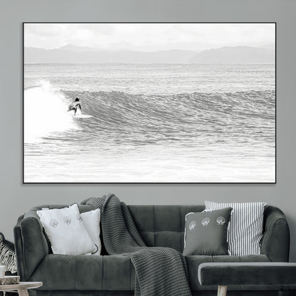 Monochrome photo of a surfer riding a wave with distant mountains, ideal for coastal motion or black and white surf-themed wall decor.