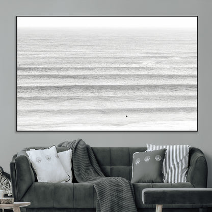 Monochrome photo of a lone surfer in calm layered waves, perfect for minimalist coastal or moody ocean-inspired wall decoration.
