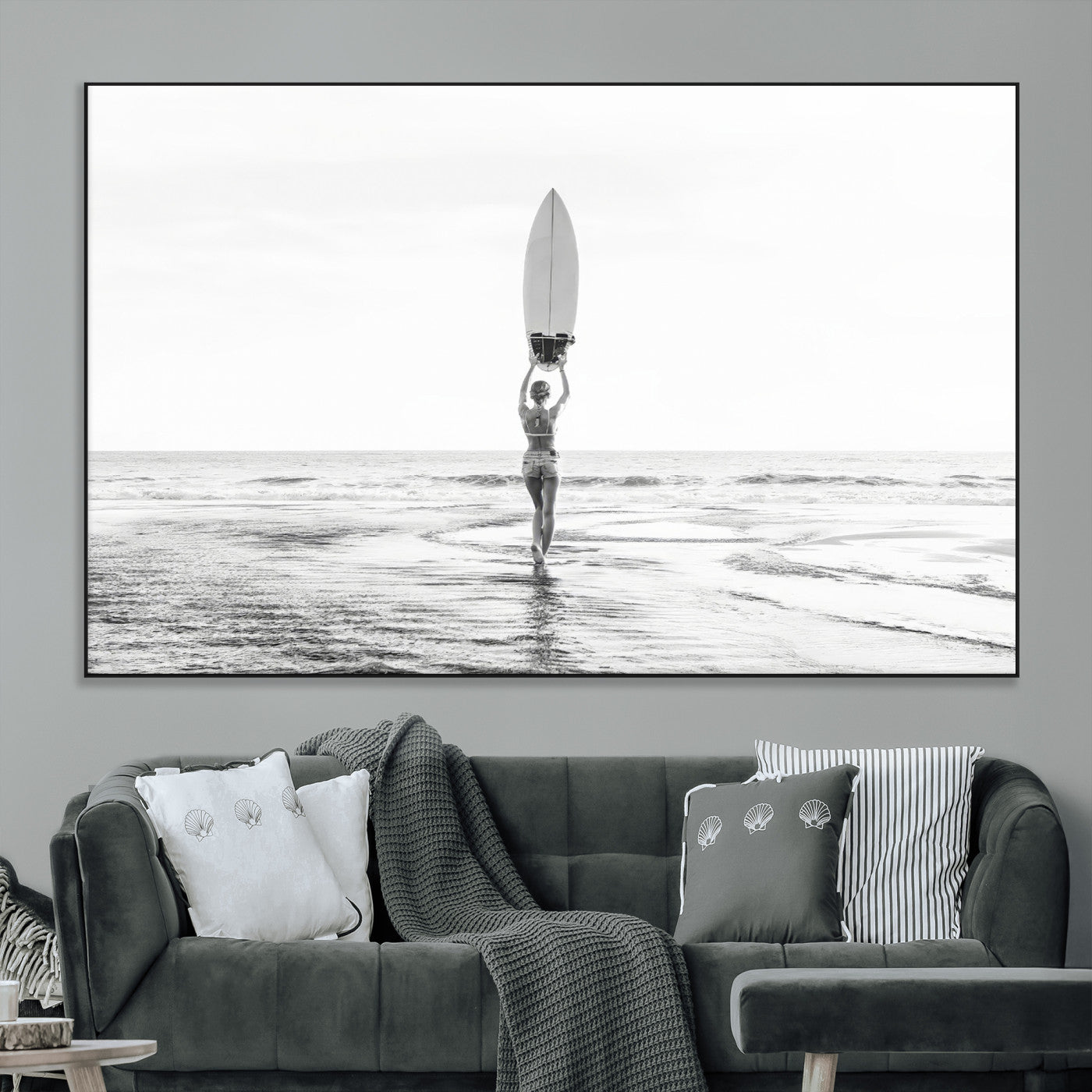 Black and white image of a female surfer holding a surfboard above her head while walking toward the ocean, creating a minimalist and bold coastal aesthetic.