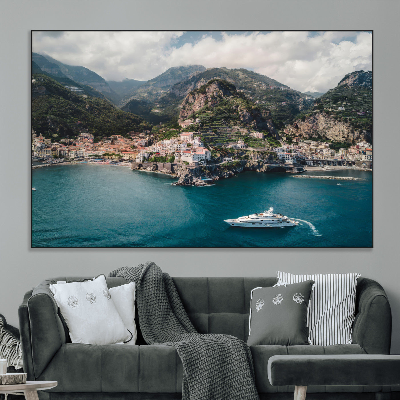 Aerial view of Amalfi Coast, Italy, with colorful hillside houses, lush green mountains, and a luxury yacht sailing in turquoise waters.