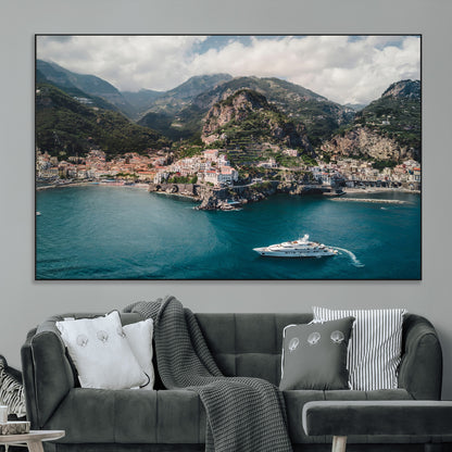 Aerial view of Amalfi Coast, Italy, with colorful hillside houses, lush green mountains, and a luxury yacht sailing in turquoise waters.