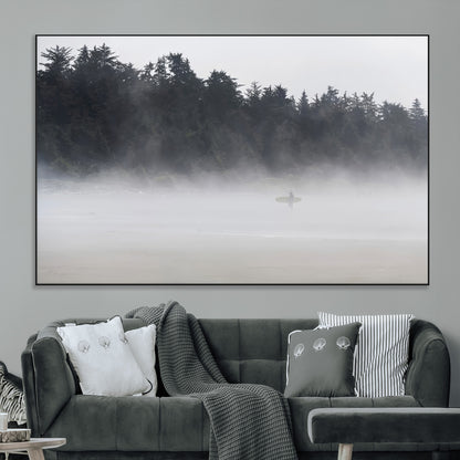 A lone surfer carrying a board through a misty shoreline, surrounded by dense trees and fog, creating a peaceful and mysterious coastal scene.