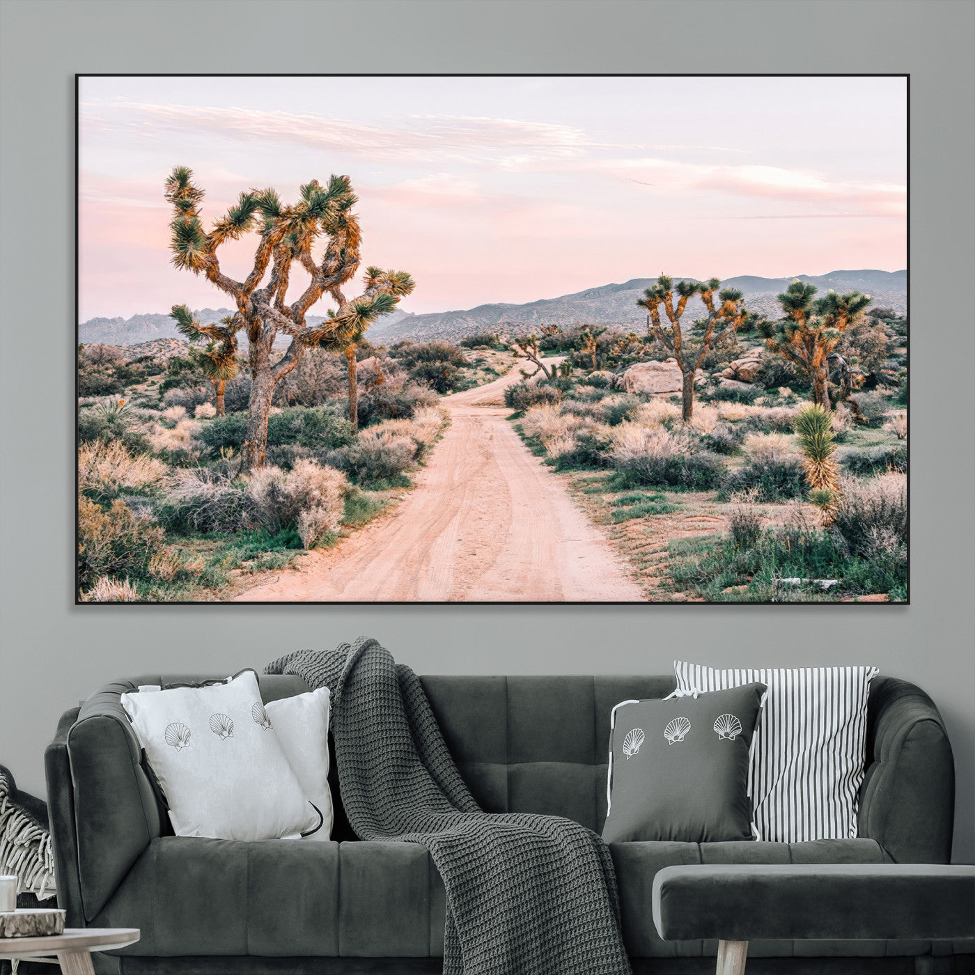 A dusty road winding through Joshua Tree National Park, framed by iconic twisted trees and warm desert tones under a soft pastel sky.