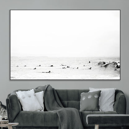 A group of surfers floating in the ocean, waiting for waves under a vast, moody sky, captured in black and white.