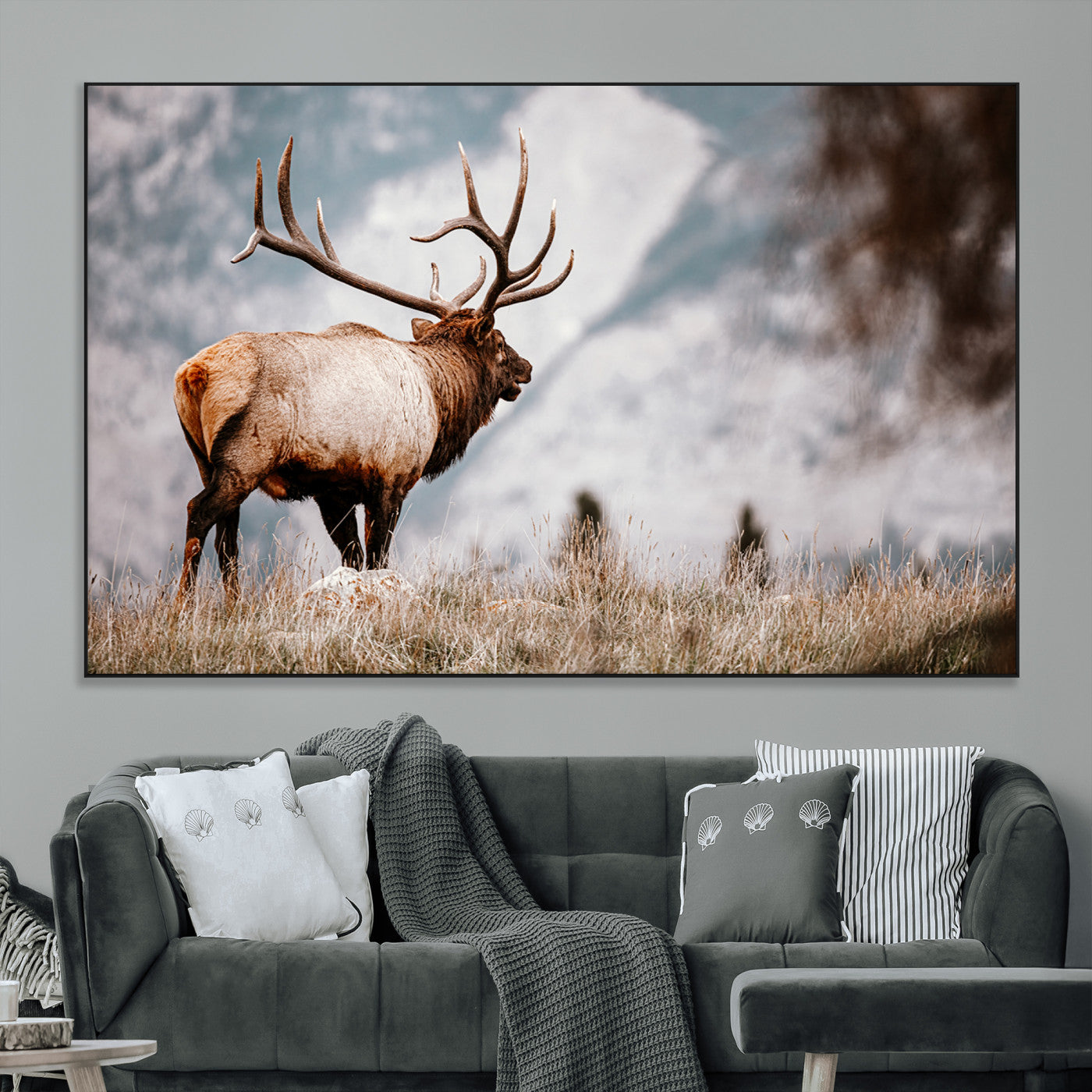 Majestic elk with large antlers standing in grass with snowy mountains in background, perfect for rustic cabin or lodge style decor.