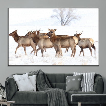 A group of elk standing on snowy terrain with a tree in the background, perfect for rustic or lodge-style winter wall decor.