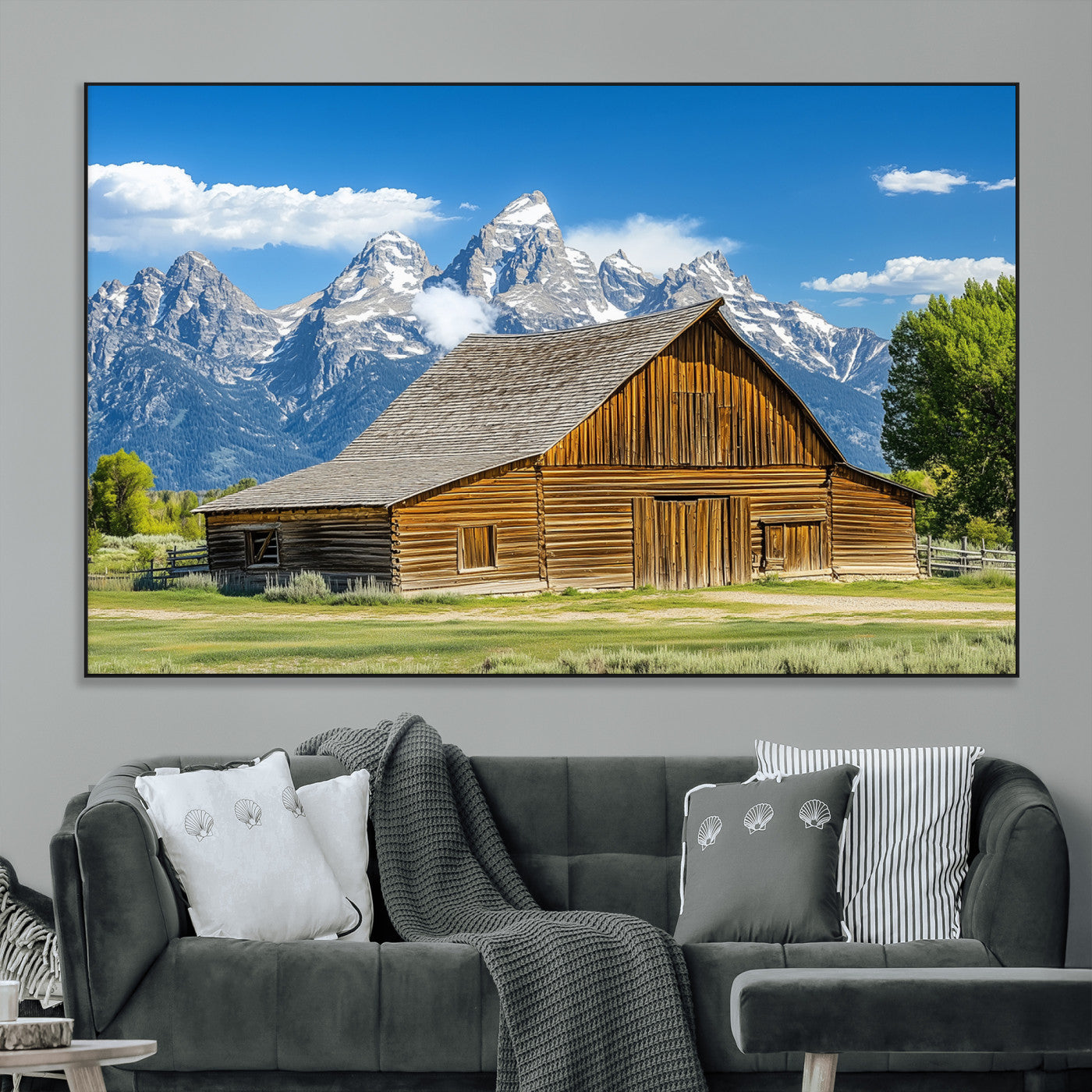A rustic wooden barn sits in front of towering mountain peaks under a clear blue sky, perfect for farmhouse or cabin style interiors.