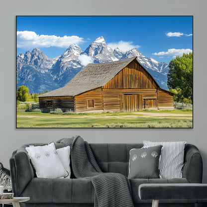 A rustic wooden barn sits in front of towering mountain peaks under a clear blue sky, perfect for farmhouse or cabin style interiors.