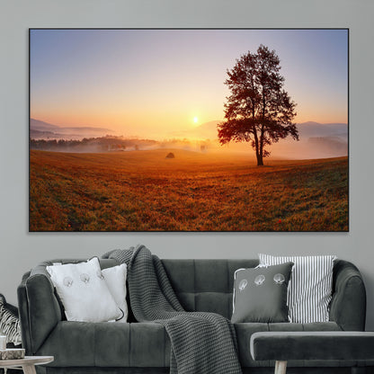 A tranquil landscape at sunrise with a mist-covered field and a lone tree, creating a peaceful and natural atmosphere.