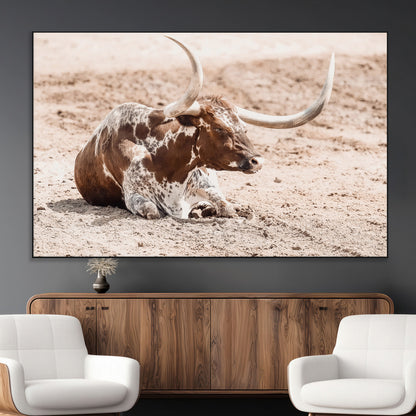 Texas Longhorn bull resting on dusty ground with warm tones, ideal for rustic western or farmhouse-themed wall decor.