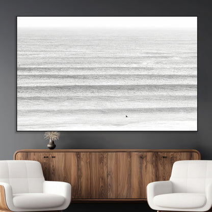 Monochrome photo of a lone surfer in calm layered waves, perfect for minimalist coastal or moody ocean-inspired wall decoration.