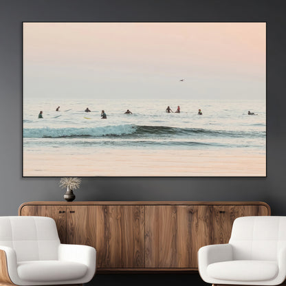 Dreamy photo of surfers waiting on soft pastel waves under a pink sunset sky, ideal for soft coastal minimalist or serene ocean-themed home decor.