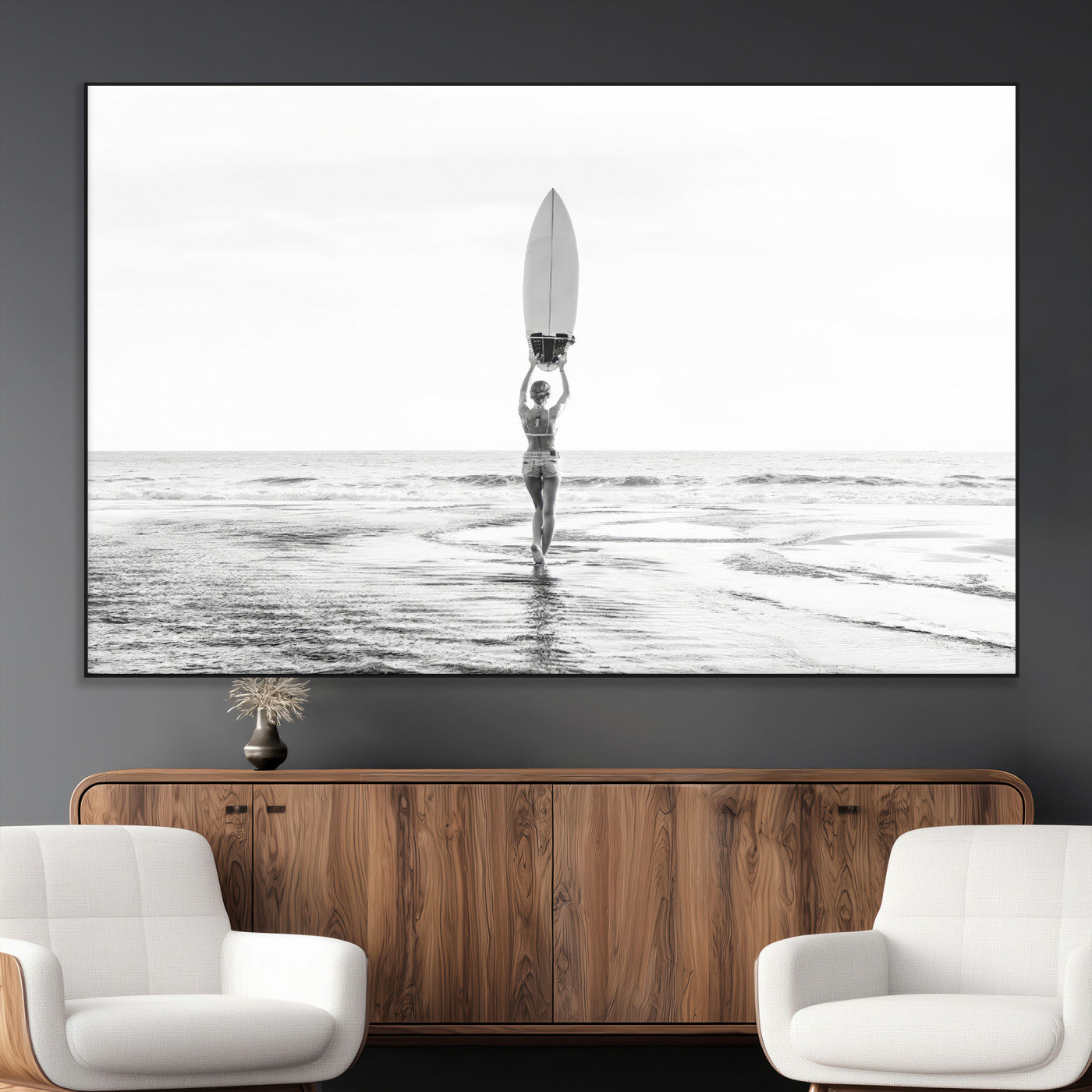 Black and white image of a female surfer holding a surfboard above her head while walking toward the ocean, creating a minimalist and bold coastal aesthetic.