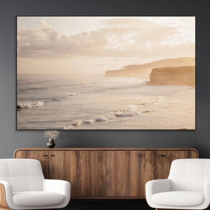 Golden hour seascape with misty cliffs and gentle waves rolling towards the shore, capturing a tranquil and warm coastal atmosphere.
