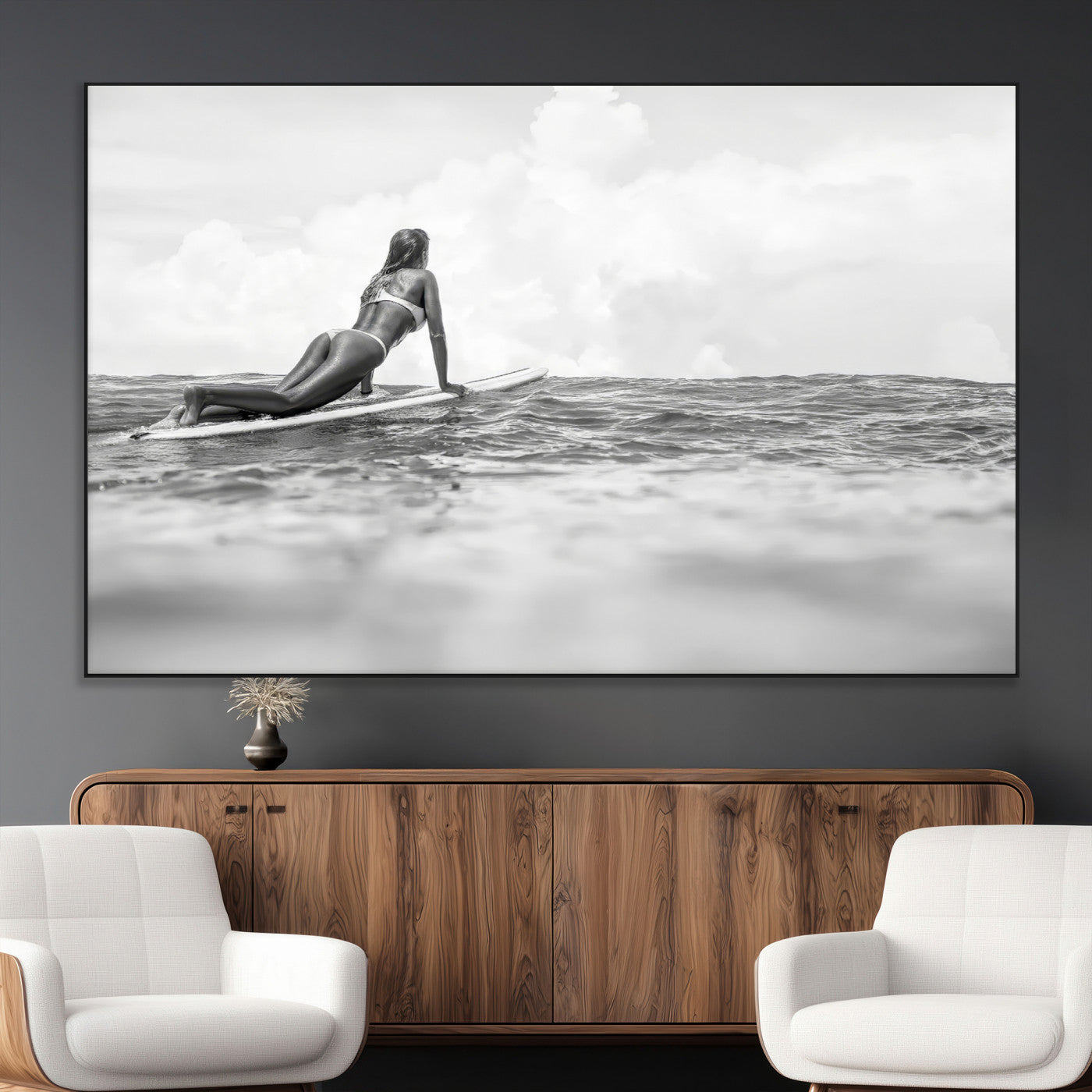 A black and white ocean scene featuring a surfer girl waiting on her board, gazing at the horizon, capturing a tranquil and adventurous coastal moment.