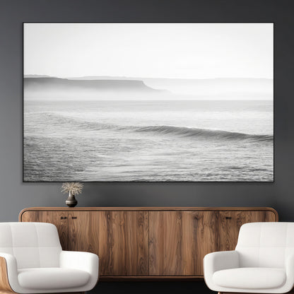 A black and white minimalist seascape featuring soft rolling waves and misty distant cliffs, creating a serene and timeless coastal atmosphere.