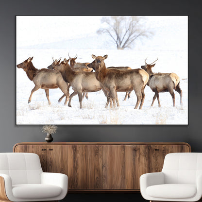 A group of elk standing on snowy terrain with a tree in the background, perfect for rustic or lodge-style winter wall decor.