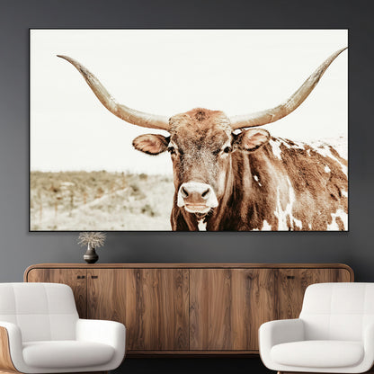 A Texas longhorn bull with wide horns, standing in a dry field under soft light, ideal for rustic farmhouse or western-themed interiors.