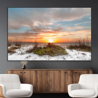 A tranquil beach scene featuring golden sunset hues over the water, with grasses in the foreground and a peaceful, serene atmosphere.