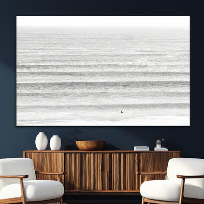 Monochrome photo of a lone surfer in calm layered waves, perfect for minimalist coastal or moody ocean-inspired wall decoration.