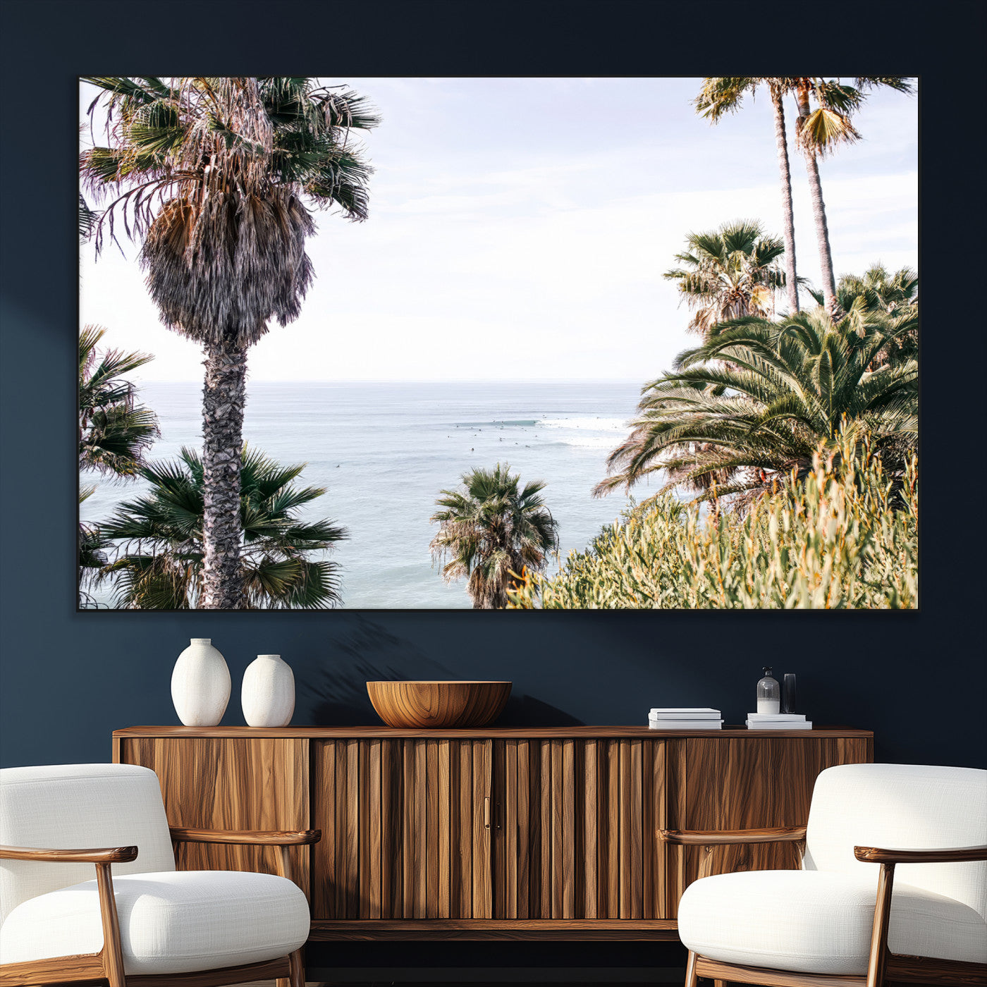 Scenic coastal view with tall palm trees overlooking a calm ocean, soft blue waves, and surfers in the distance, creating a peaceful tropical vibe.