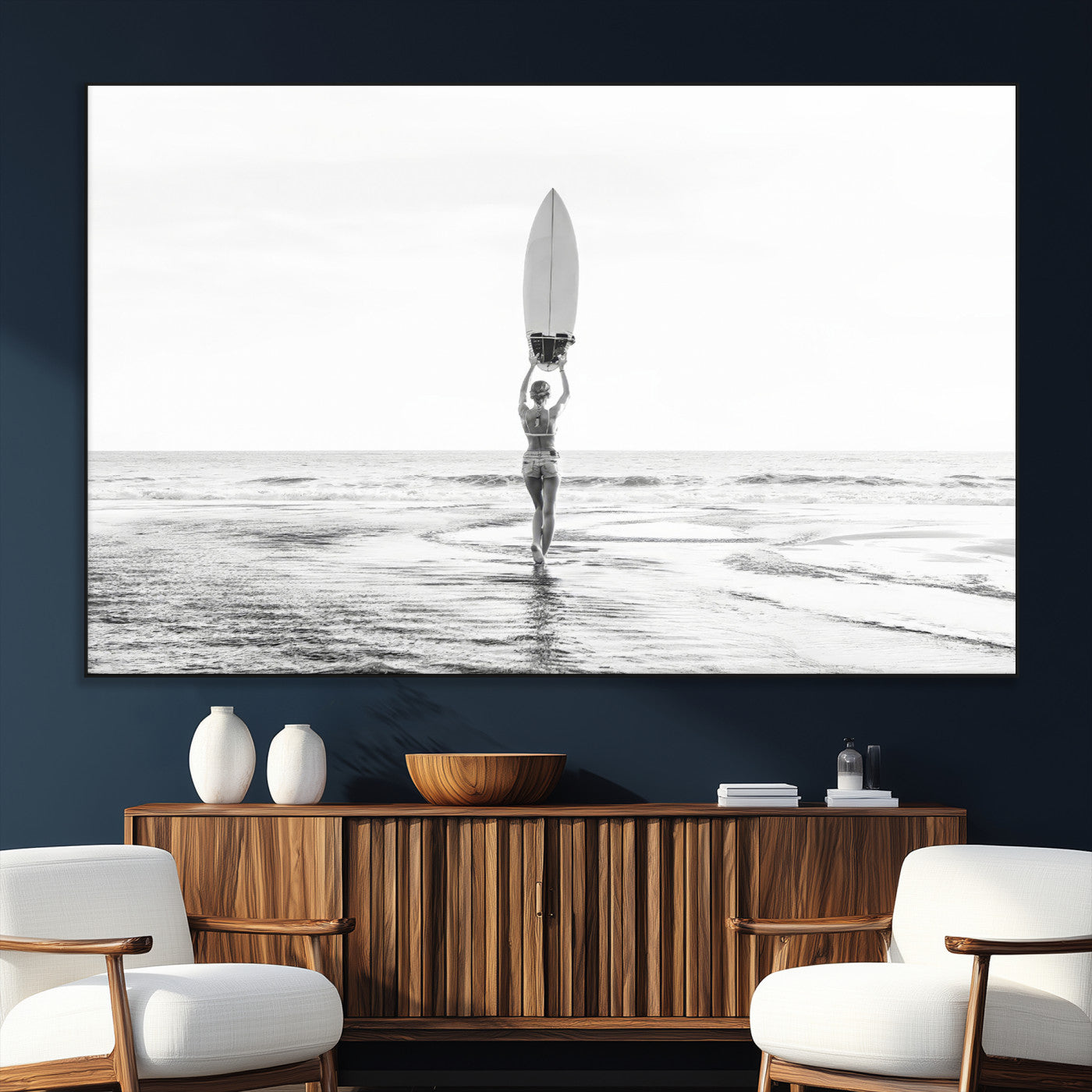 Black and white image of a female surfer holding a surfboard above her head while walking toward the ocean, creating a minimalist and bold coastal aesthetic.