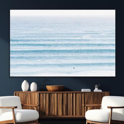 Minimalist ocean view with soft blue waves and a lone surfer, creating a serene and airy coastal aesthetic, perfect for tranquil home decor.