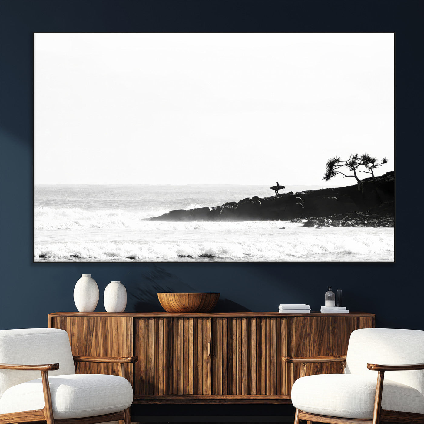 Black and white photo of a surfer standing on rocky cliffs, gazing at the waves, embodying the spirit of adventure and solitude.