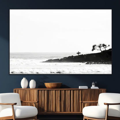 Black and white photo of a surfer standing on rocky cliffs, gazing at the waves, embodying the spirit of adventure and solitude.