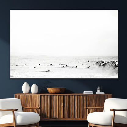 A group of surfers floating in the ocean, waiting for waves under a vast, moody sky, captured in black and white.