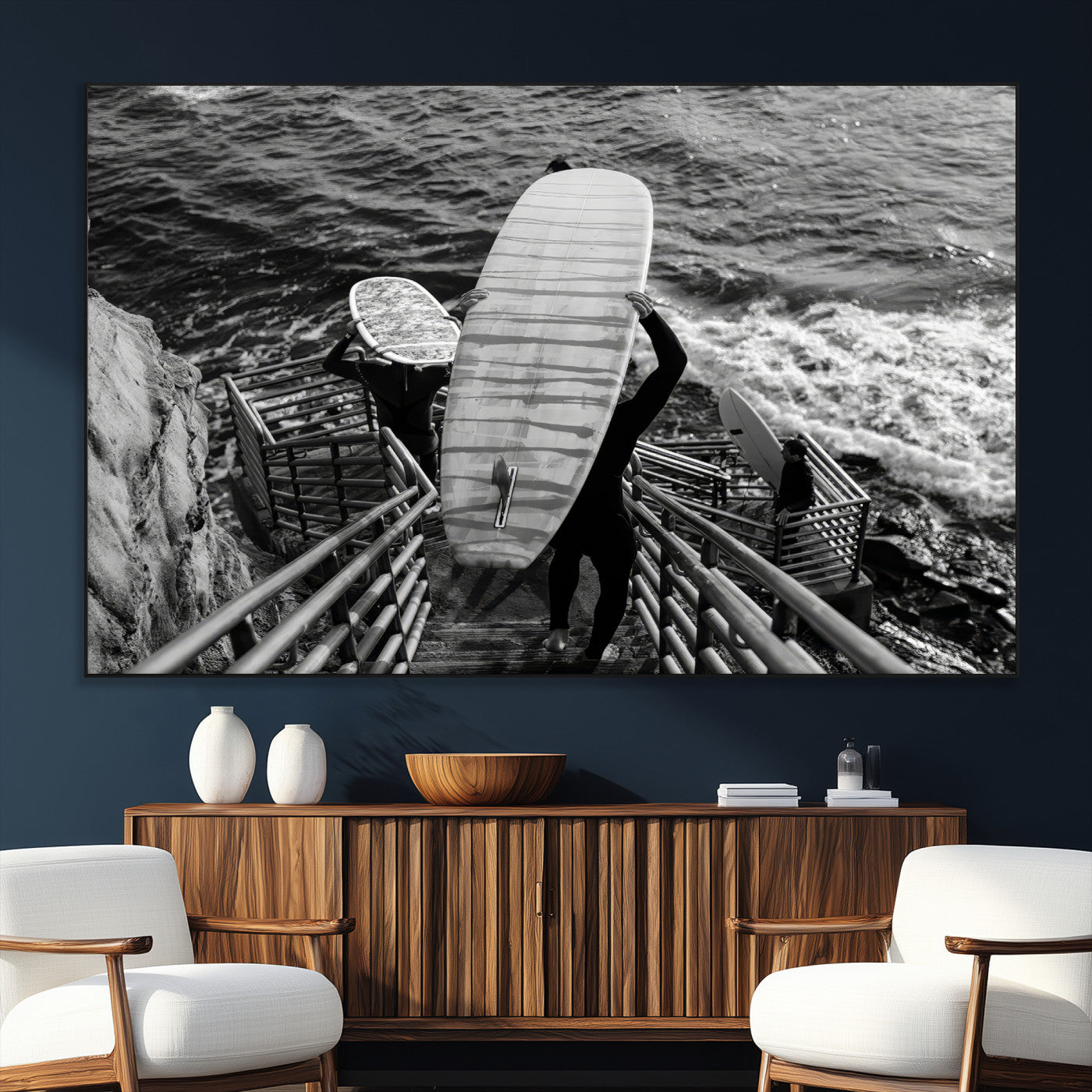 Black and white photo of surfers carrying boards down a rugged cliffside stairway, capturing a bold and adventurous coastal scene.