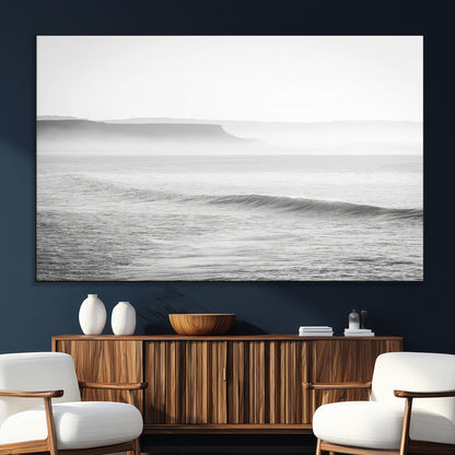 A black and white minimalist seascape featuring soft rolling waves and misty distant cliffs, creating a serene and timeless coastal atmosphere.
