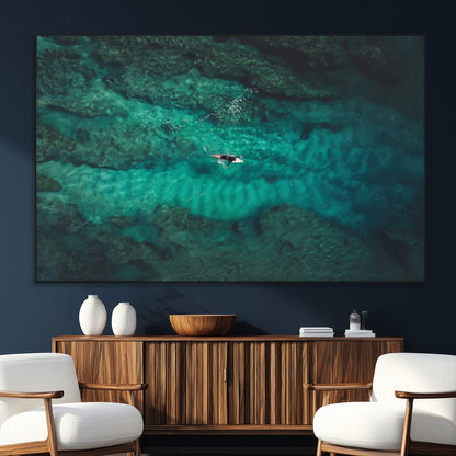 An aerial view of a solo surfer paddling through crystal-clear turquoise waters over a sunlit reef, capturing the beauty and serenity of open water surfing.