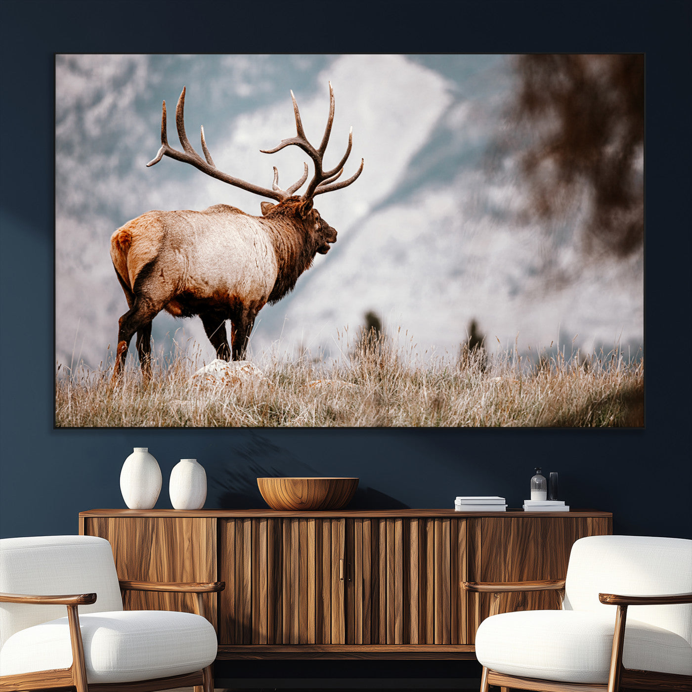 Majestic elk with large antlers standing in grass with snowy mountains in background, perfect for rustic cabin or lodge style decor.