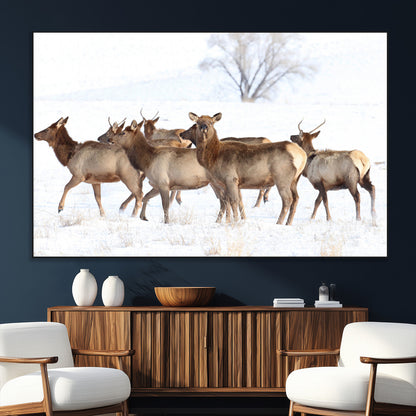 A group of elk standing on snowy terrain with a tree in the background, perfect for rustic or lodge-style winter wall decor.