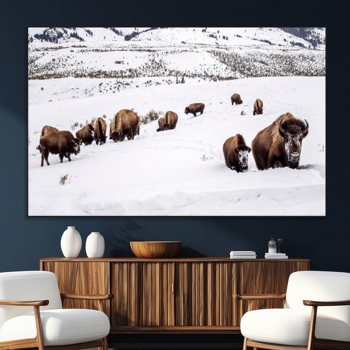 A herd of bison walking through deep snow in a mountain valley, perfect for rustic, cabin or western-themed wall decor.