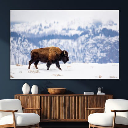 A lone bison walks across snowy ground with blue-toned mountain range behind, ideal for rustic or western farmhouse interiors.