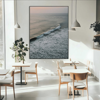 Aerial view of ocean waves rolling towards the shore under a soft sunset sky, creating a peaceful and minimalist coastal scene.