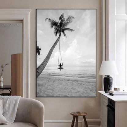 Monochrome photo of a woman swinging from a palm tree on a serene beach, ideal for minimalist or tropical coastal decor.