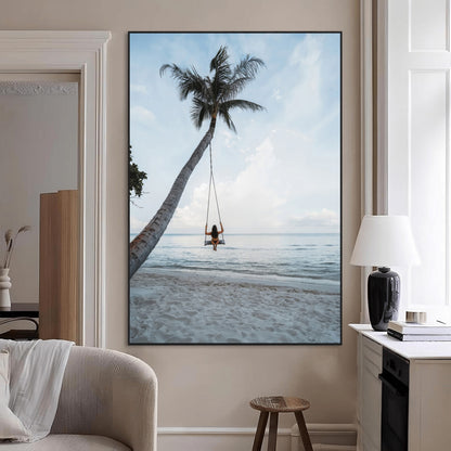 Wall art of a girl on a swing hanging from a palm tree over calm ocean waters, perfect for tropical or minimalist coastal decor.