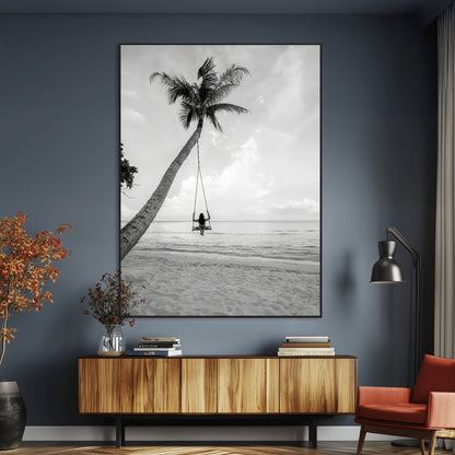 Monochrome photo of a woman swinging from a palm tree on a serene beach, ideal for minimalist or tropical coastal decor.