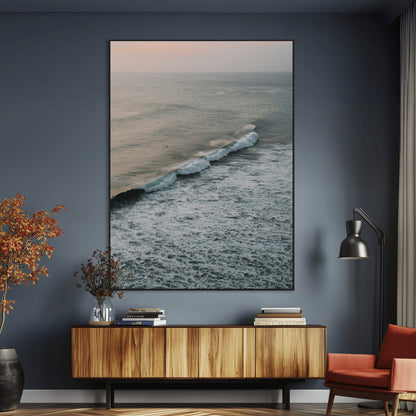 Aerial view of ocean waves rolling towards the shore under a soft sunset sky, creating a peaceful and minimalist coastal scene.